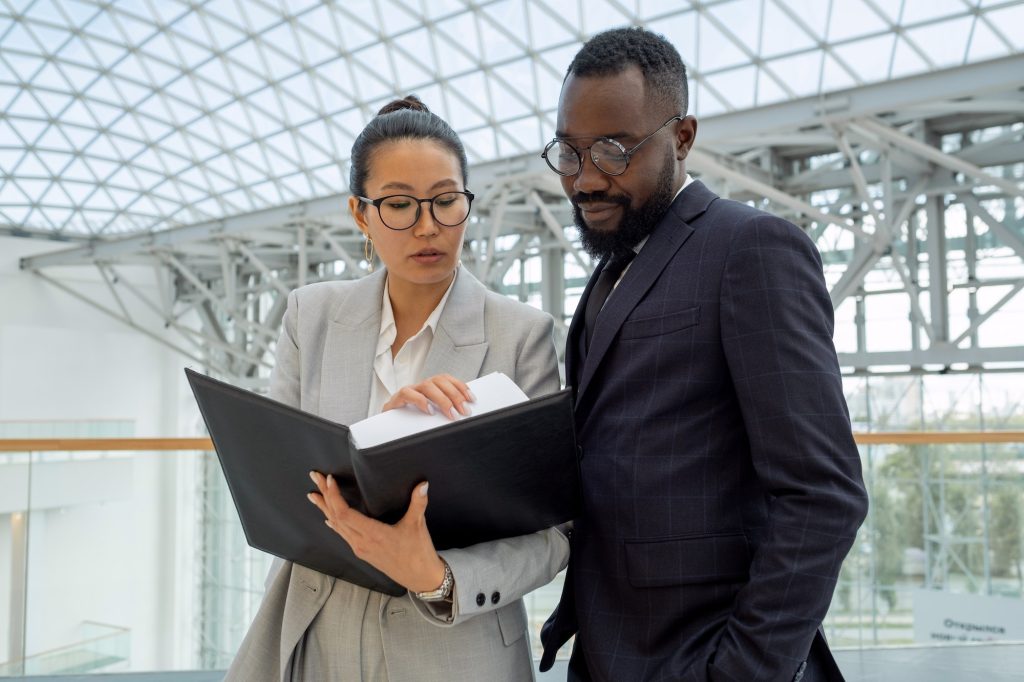 Young businesswoman showing financial papers or contract to African colleague